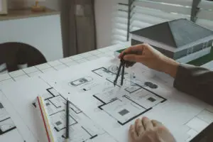 An architect is working in the office, there are blueprint and house model on the desk, engineer is checking overall of work that going to be present one last time, using tool for making work easier