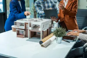 architect-engineer team discusses modern house model at desk. They review renovation project.