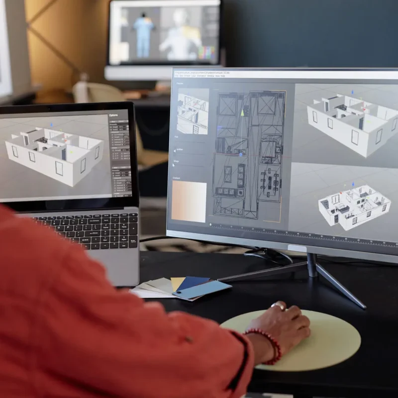 Person analyzing architectural designs on computer screens at office workspace, focusing on detailed models and layouts for a project. Engaging in work through high-end technology